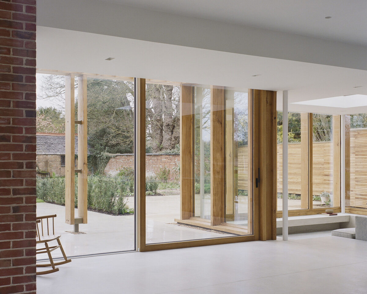 Modern interior pergola house with large floor-to-ceiling wooden-framed windows overlooking a garden.